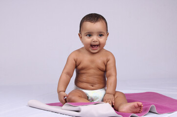 Happy looking infant Indian baby sitting in a diaper after being oil massaged.