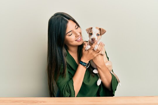 Young hispanic girl smiling happy and hugging dog sitting on the table over isolated white background.