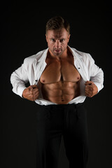 Strong man show fit abdominal muscles in open shirt formal style black background, abs