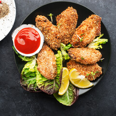 Appetizing crispy chicken wings breaded with bread crumbs with lettuce, sauce, lemon, microgreens in a plate on the table. Top view