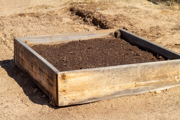 A wooden raised garden bed on sand ground