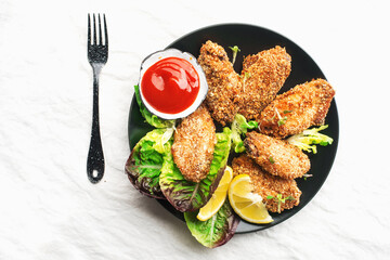 Appetizing crispy chicken wings breaded with bread crumbs with lettuce, sauce, lemon, microgreens in a plate on the table. Top view