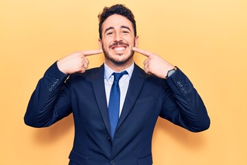 Young hispanic man wearing suit smiling cheerful showing and pointing with fingers teeth and mouth. dental health concept.