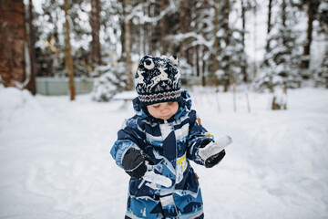 Fototapeta na wymiar little cute caucasian boy holding icicles wearing winter overall in the countryside. Image with selective focus