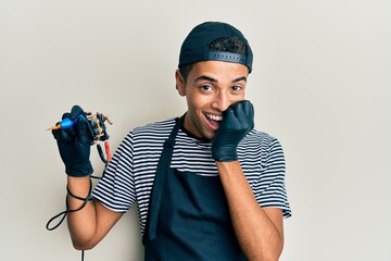 Young handsome african american man tattoo artist wearing professional uniform and gloves holding...