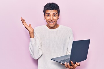 Young african amercian man holding laptop celebrating victory with happy smile and winner expression with raised hands