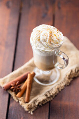 Pumpkin spice latte in a glass mug. Pumpkin latte with whipped cream and spices on a wooden background. Hot autumn coffee drink on a burlap
