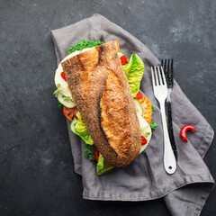 Half a baguette for a snack, lunch, dinner, sandwich with mozzarella cheese, fresh vegetables and lettuce with hot peppers on a dark background. Top view. Simple comfort food,