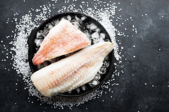 Fillet of white sea cold-water fish cod in ice cubes on a dark background. Top view