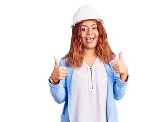 Young latin woman wearing architect hardhat success sign doing positive gesture with hand, thumbs up smiling and happy. cheerful expression and winner gesture.