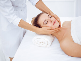 Fototapeta na wymiar Young and blonde woman enjoying facial massage in spa salon. Beauty concept