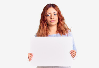 Fototapeta premium Young latin woman holding blank empty banner thinking attitude and sober expression looking self confident