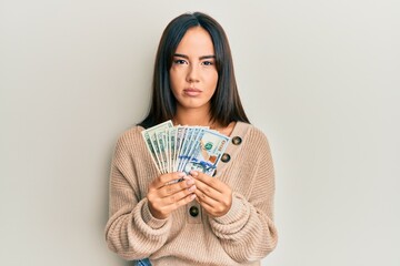 Young beautiful hispanic girl holding dollars relaxed with serious expression on face. simple and natural looking at the camera.