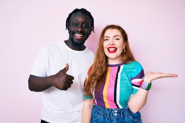 Interracial couple wearing casual clothes showing palm hand and doing ok gesture with thumbs up, smiling happy and cheerful