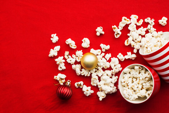 Homemade popcorn for a festive treat in red Christmas mugs with shiny New Year's red and gold Christmas decorations balls. Top view. Festive atmosphere picture. Top view,