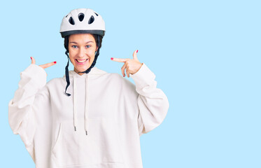 Beautiful brunette young woman wearing bike helmet and sporty clothes smiling cheerful showing and pointing with fingers teeth and mouth. dental health concept.