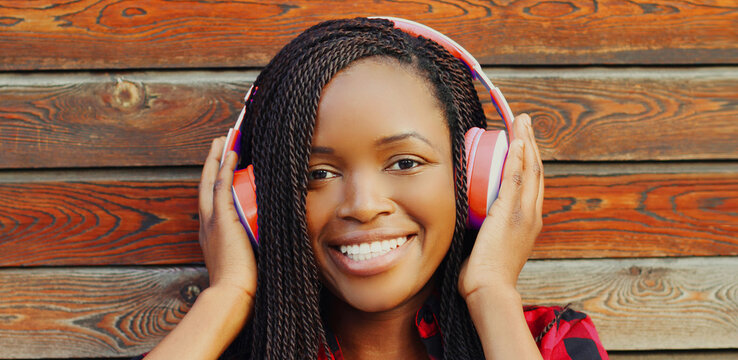 Portrait of happy young smiling african woman in wireless headphones over city background