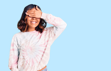 Young beautiful mixed race woman wearing casual tie dye sweatshirt smiling and laughing with hand on face covering eyes for surprise. blind concept.