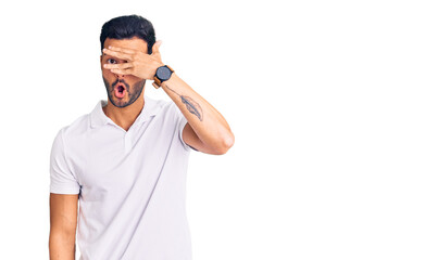 Fototapeta premium Young handsome hispanic man wearing casual clothes peeking in shock covering face and eyes with hand, looking through fingers with embarrassed expression.