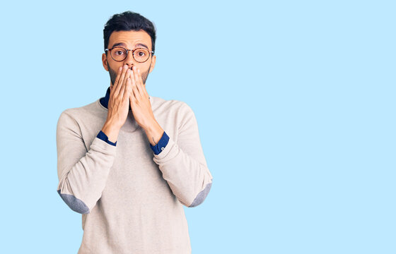 Young handsome hispanic man wearing elegant clothes and glasses shocked covering mouth with hands for mistake. secret concept.