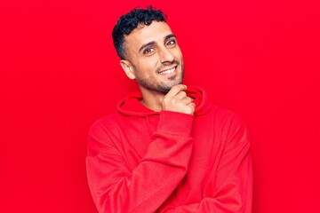 Young hispanic man wearing casual clothes smiling looking confident at the camera with crossed arms and hand on chin. thinking positive.