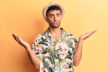 Young hispanic man wearing summer hat clueless and confused with open arms, no idea and doubtful face.