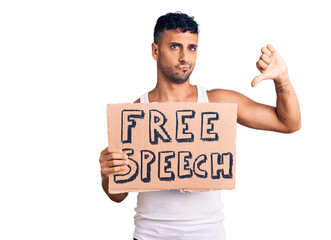 Young hispanic man holding free speech banner with angry face, negative sign showing dislike with thumbs down, rejection concept