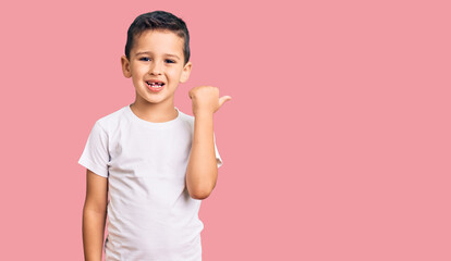 Little cute boy kid wearing casual white tshirt smiling with happy face looking and pointing to the side with thumb up.