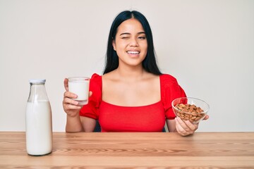 Young asian girl drinking healthy almond milk winking looking at the camera with sexy expression,...