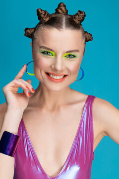 Portrait of beautiful young female model with neon makeup and stylish hair, wearing shiny swimsuit. Smiling happy girl posing in studio. 