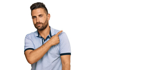 Handsome man with beard wearing casual clothes pointing with hand finger to the side showing advertisement, serious and calm face