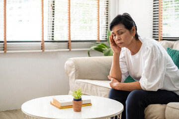 Senior old Asian woman feel stressed, headache sitting alone on sofa at home