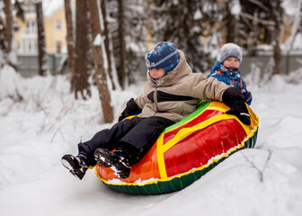 handsome caucasian boy wearing winter clothing sliding down on tubing. Another boy sitting on snow slide behind him