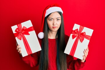 Young chinese woman wearing christmas hat and holding gifts skeptic and nervous, frowning upset because of problem. negative person.