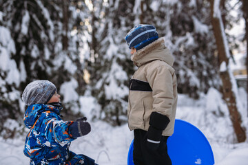 cute caucasian boys playing on fresh air on winter day, one is holding snow sled © Yulia Raneva
