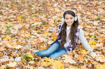 autumn kid fashion. inspiration. happy childhood. back to school. girl among maple leaves relax in park. fall beauty in forest. enjoy music in earphones. education online and e-learning