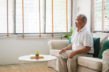 Senior old Asian man sitting on sofa practicing yoga and meditation at home, retirement and wellbeing concept