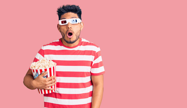 Handsome Latin American Young Man Wearing 3d Glasses And Eating Popcorn At The Movies Scared And Amazed With Open Mouth For Surprise, Disbelief Face