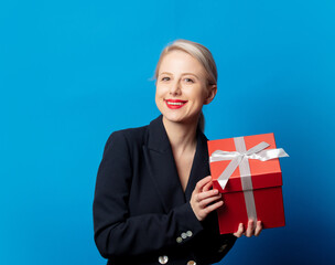 Style blonde in black jacket with gift box on blue background