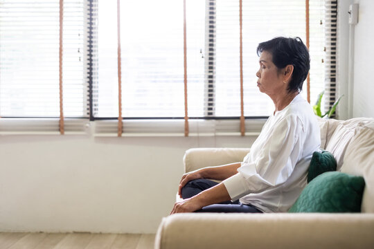 Senior Old Asian Woman Sitting On Sofa Practicing Yoga And Meditation At Home, Retirement And Wellbeing Concept