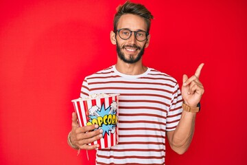 Handsome caucasian man with beard eating popcorn smiling happy pointing with hand and finger to the side