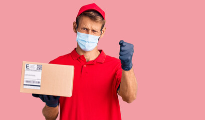 Fototapeta na wymiar Handsome blond man with beard holding delivery box wearing medical mask annoyed and frustrated shouting with anger, yelling crazy with anger and hand raised