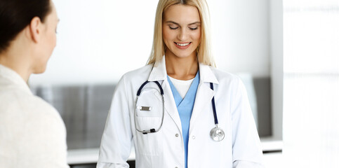 Woman-doctor at work in hospital is happy to communicate with female patient. Blonde physician checks medical history record and exam results. Medicine concept