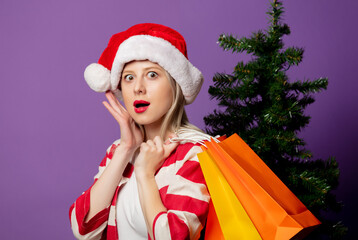 Beautiful blonde in Christmas hat and with shopping bags on puprle background