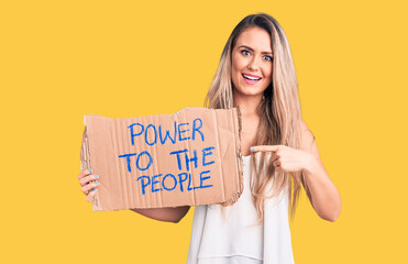 Young beautiful blonde woman holding power to the people cardboard banner smiling happy pointing with hand and finger