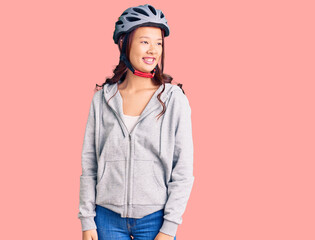 Young beautiful chinese girl wearing bike helmet looking away to side with smile on face, natural expression. laughing confident.