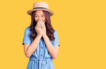 Young beautiful chinese girl wearing summer hat laughing and embarrassed giggle covering mouth with...