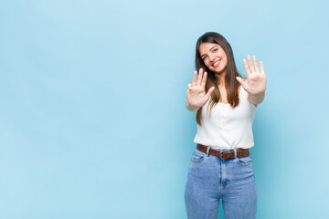 youn pretty woman smiling and looking friendly, showing number nine or ninth with hand forward,...