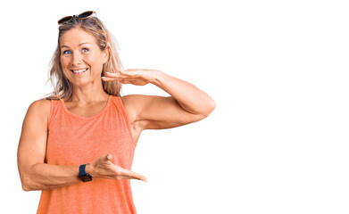 Middle age fit blonde woman wearing casual summer clothes and sunglasses gesturing with hands showing big and large size sign, measure symbol. smiling looking at the camera. measuring concept.