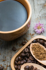 Black coffee in a cup and coffee beans in a wooden spoon on a wooden table.